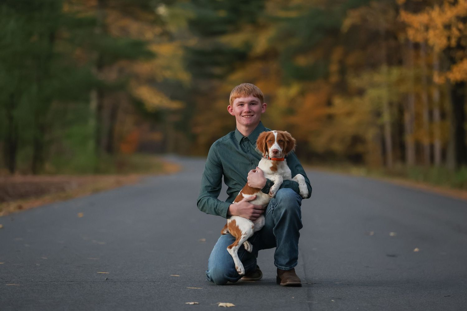 A person and beagle puppy share a tender moment on a scenic autumn road surrounded by fall foliage.