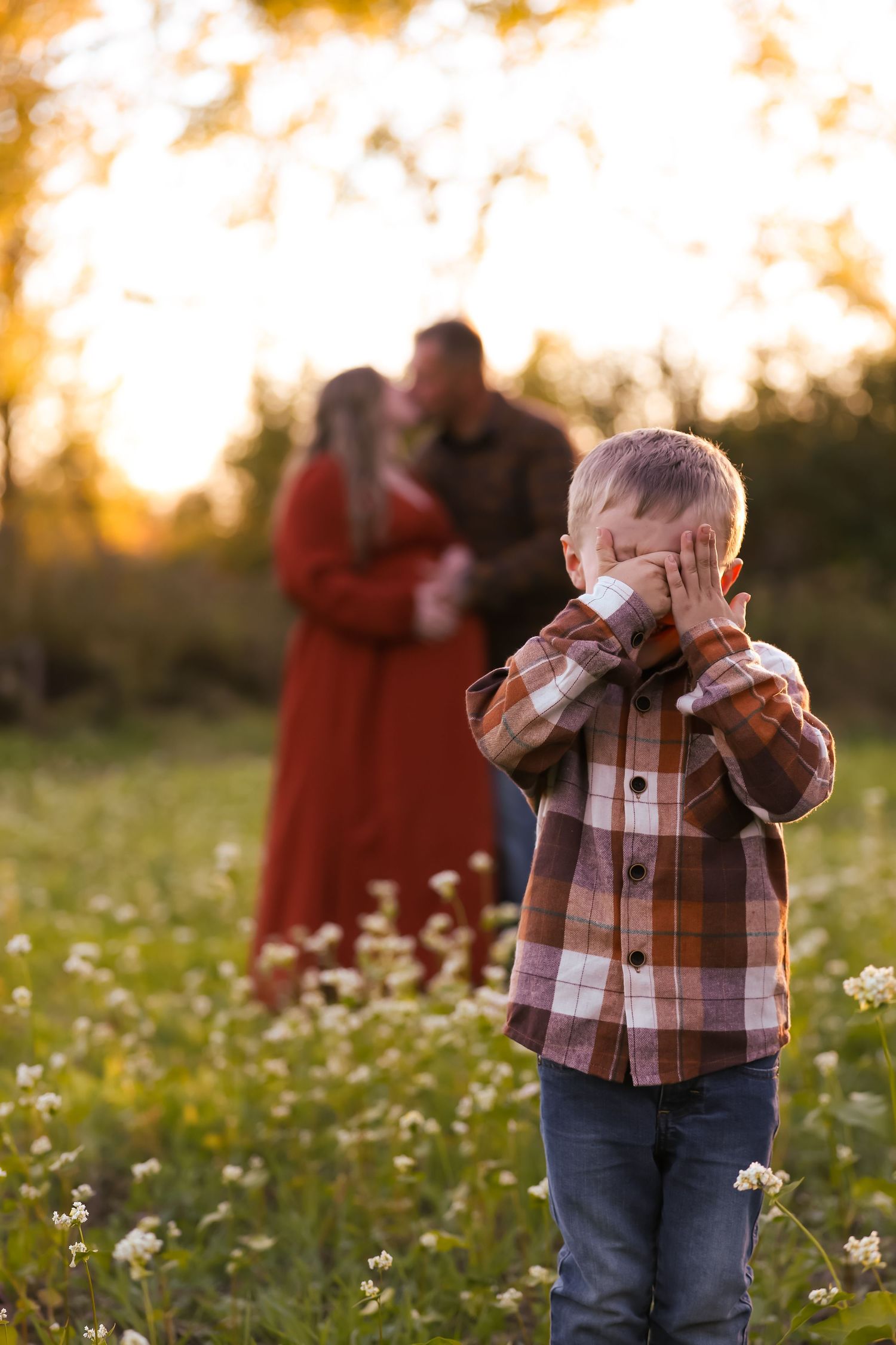 A child in a plaid shirt and jeans plays in a wildflower field during golden hour sunset.