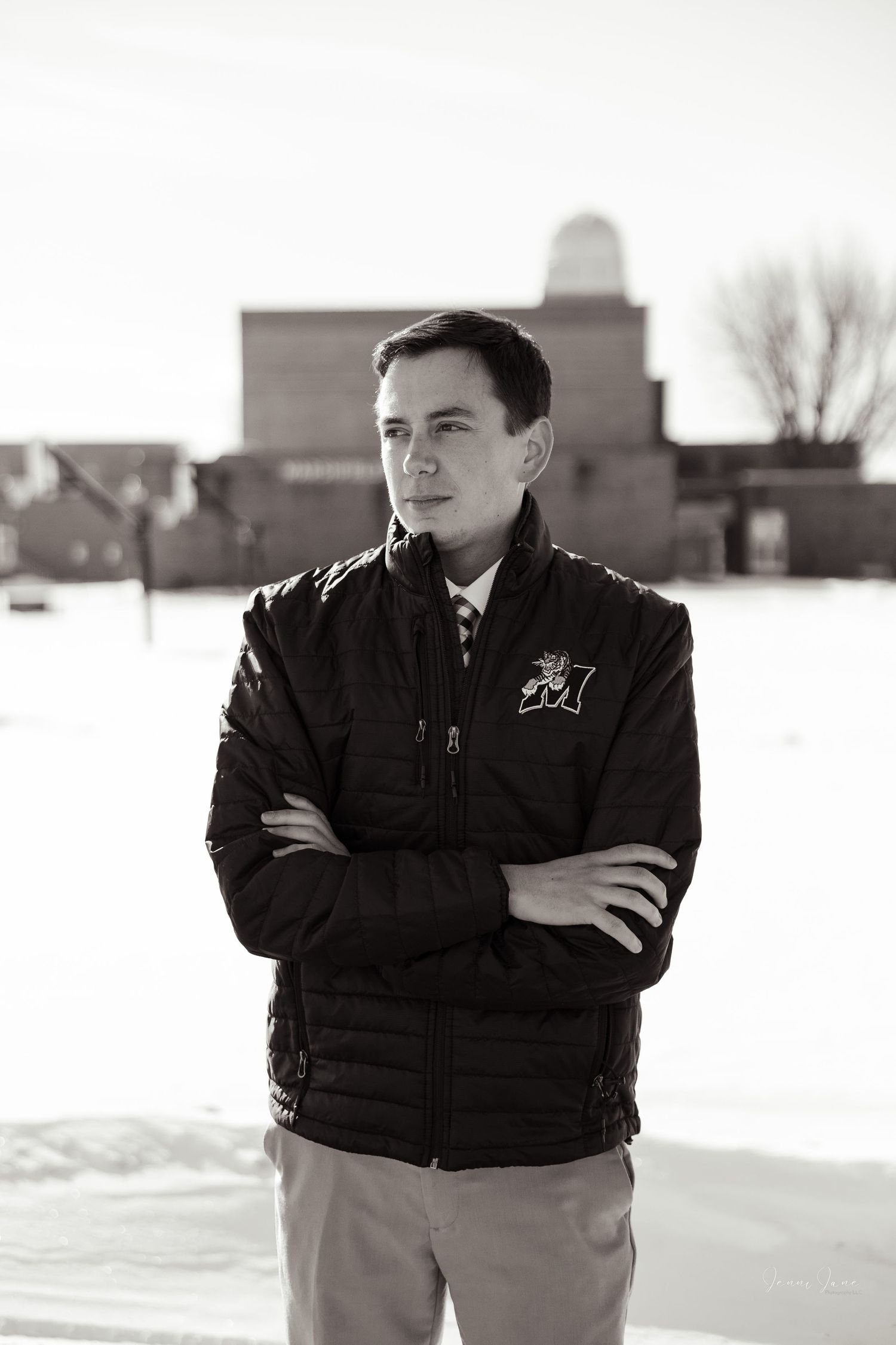 A person in a black vest stands in a snowy field with buildings visible in the background.