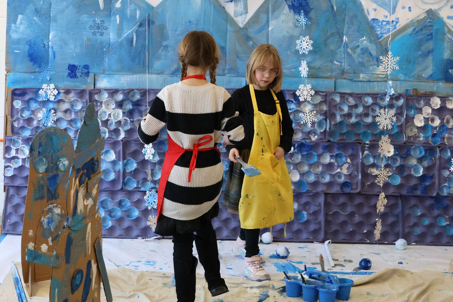 Students work on art projects in a classroom decorated with blue snowflake patterns on the walls.