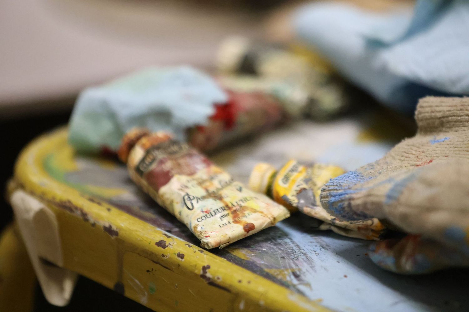 Used paint tubes and art supplies lie scattered on a yellow surface in a shallow depth of field shot.