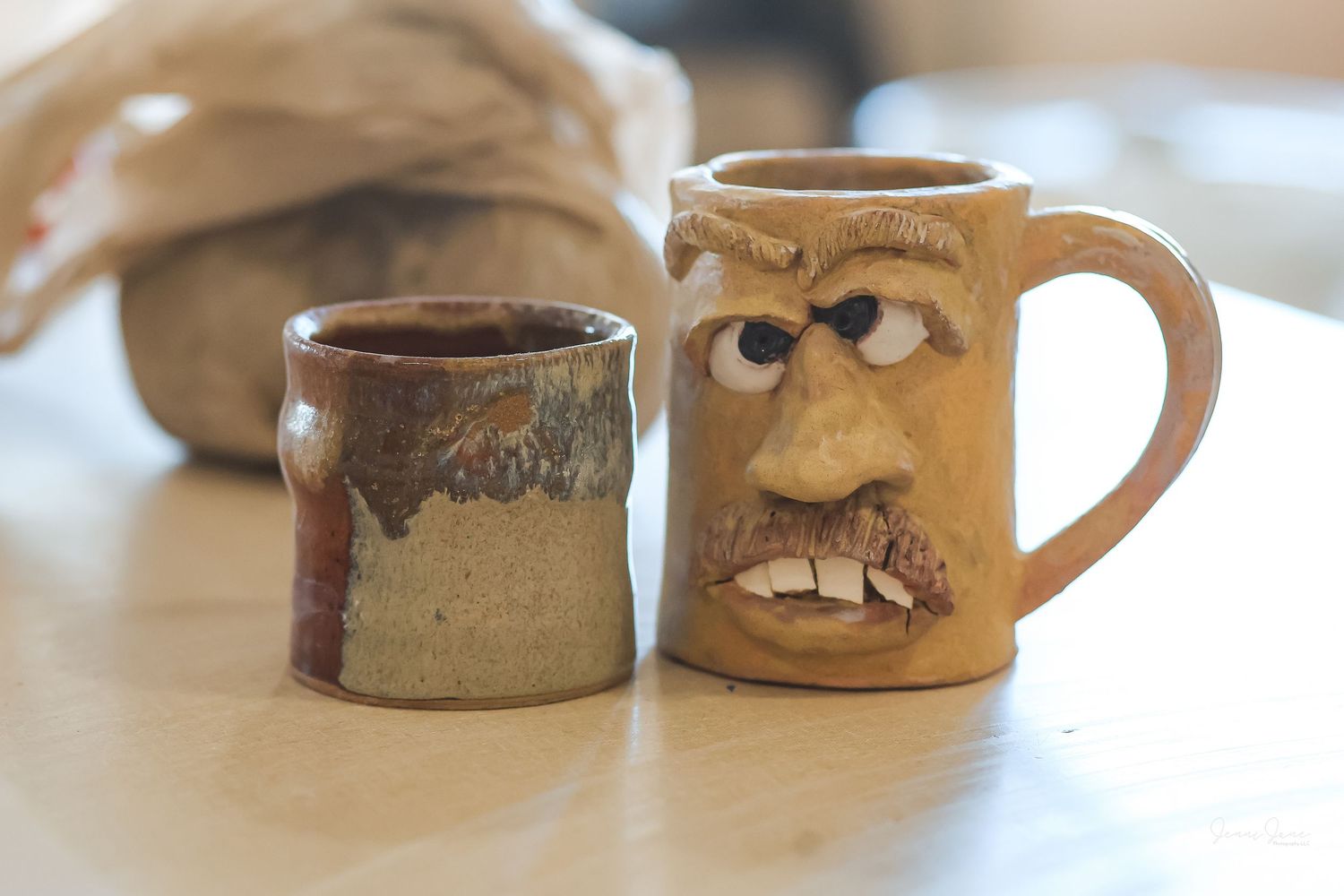 A collection of handmade ceramic coffee mugs with rustic brown and tan glazes displayed in a row on a light surface.