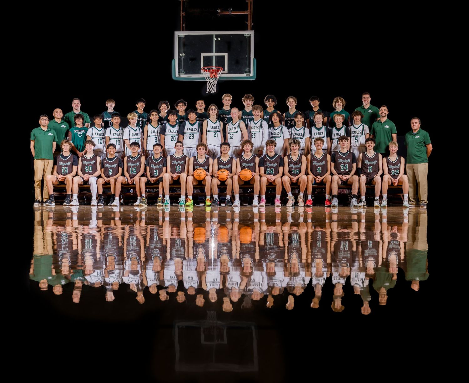 Basketball team group photo with reflective floor effect in a gymnasium setting.