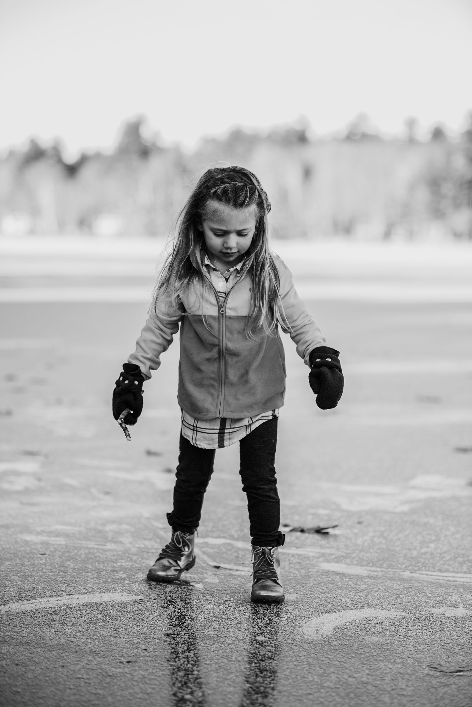 A child playing on wet pavement wearing winter clothes in black and white photography.