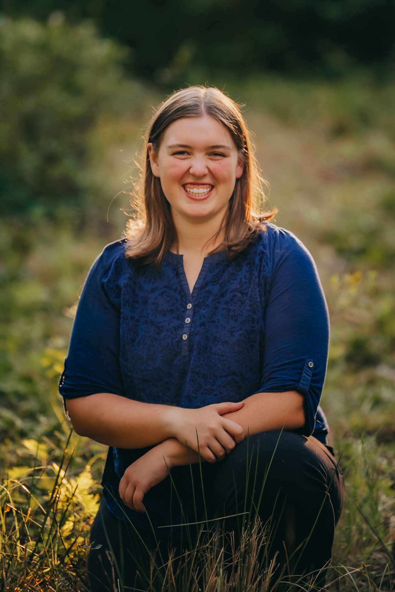 Person in dark blue top sits outdoors surrounded by golden grass and natural lighting.