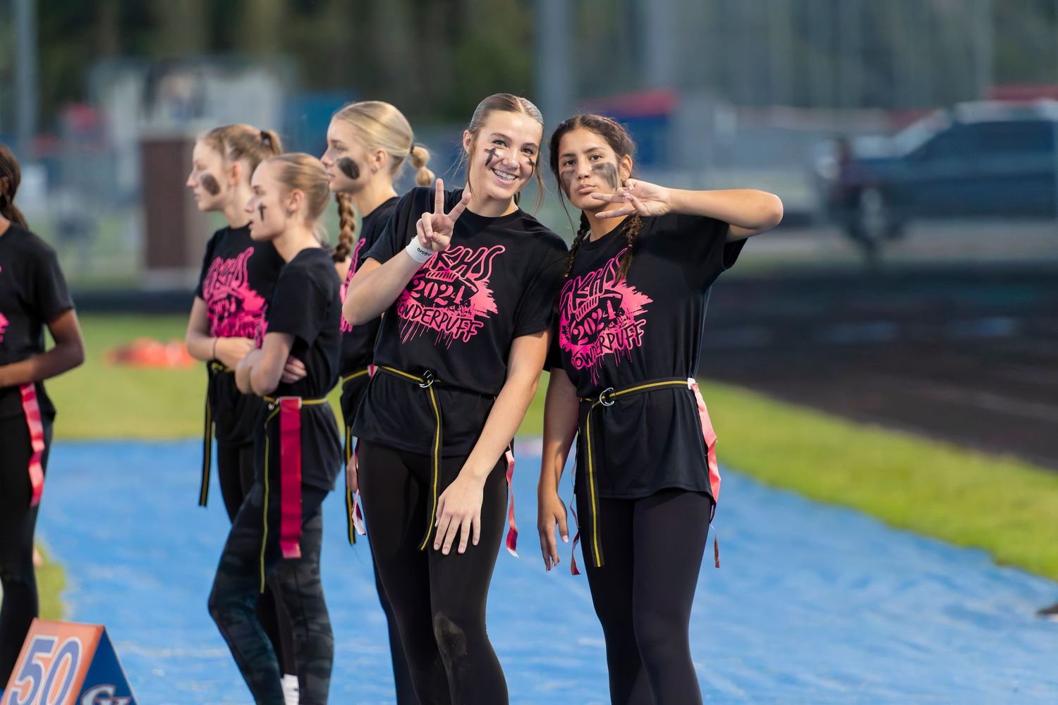 Smiling performers in black and pink uniforms pose on a field during a color guard competition.