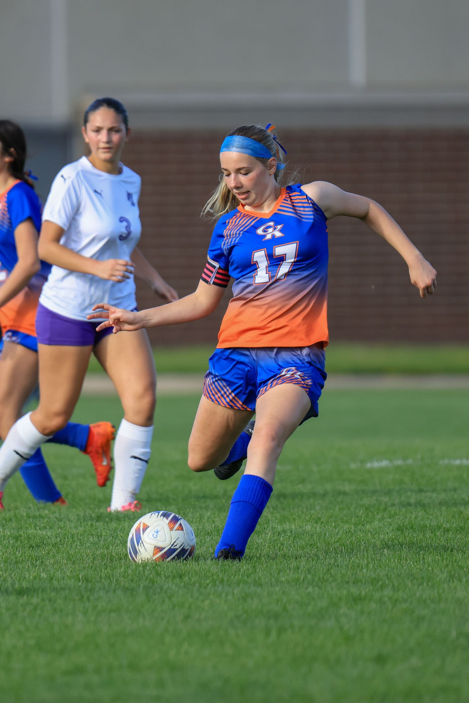 Female soccer player #17 in blue and orange uniform dribbling ball during a competitive women's soccer match.