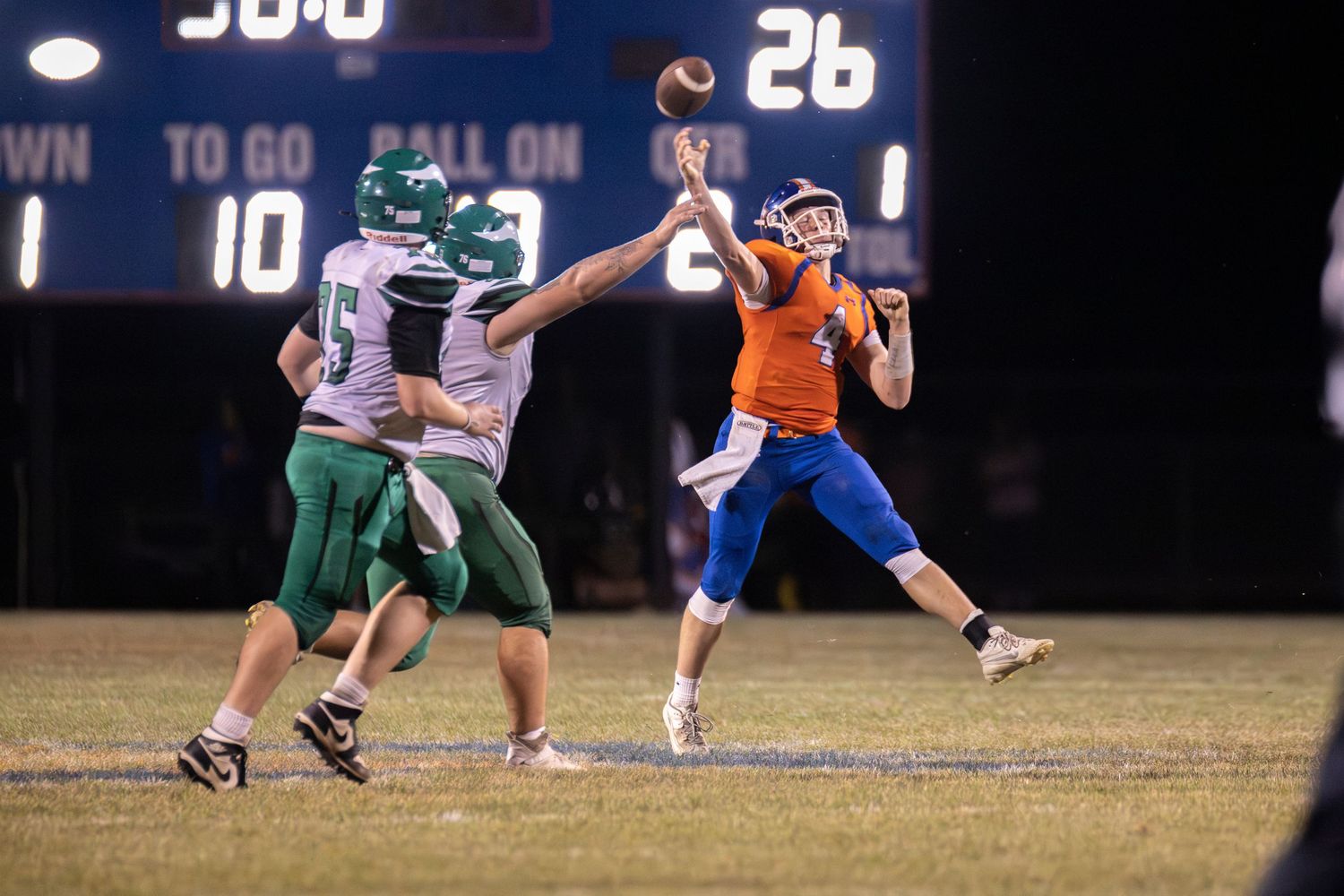 Quarterback in orange uniform throws pass under pressure during night game.