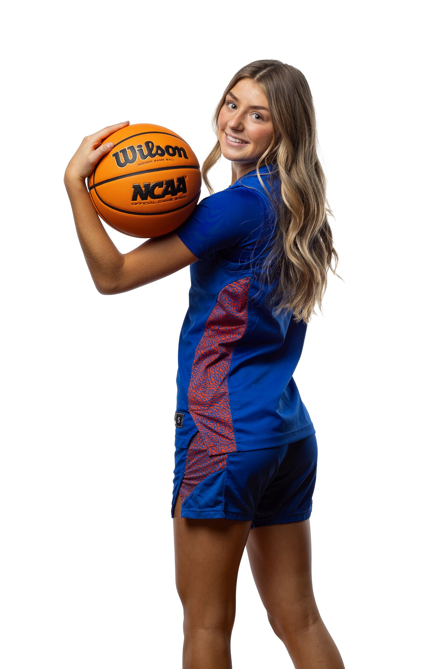Young female basketball player in blue NCAA uniform holding a Wilson basketball, posing for a portrait photo.