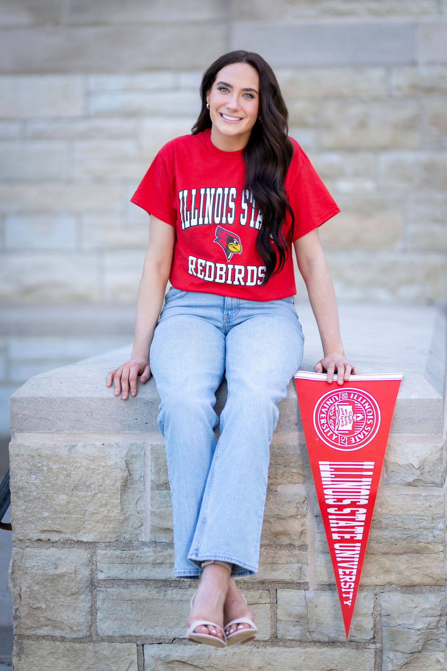 Young woman in Illinois State Redbirds red t-shirt sitting on stone steps holding ISU pennant.