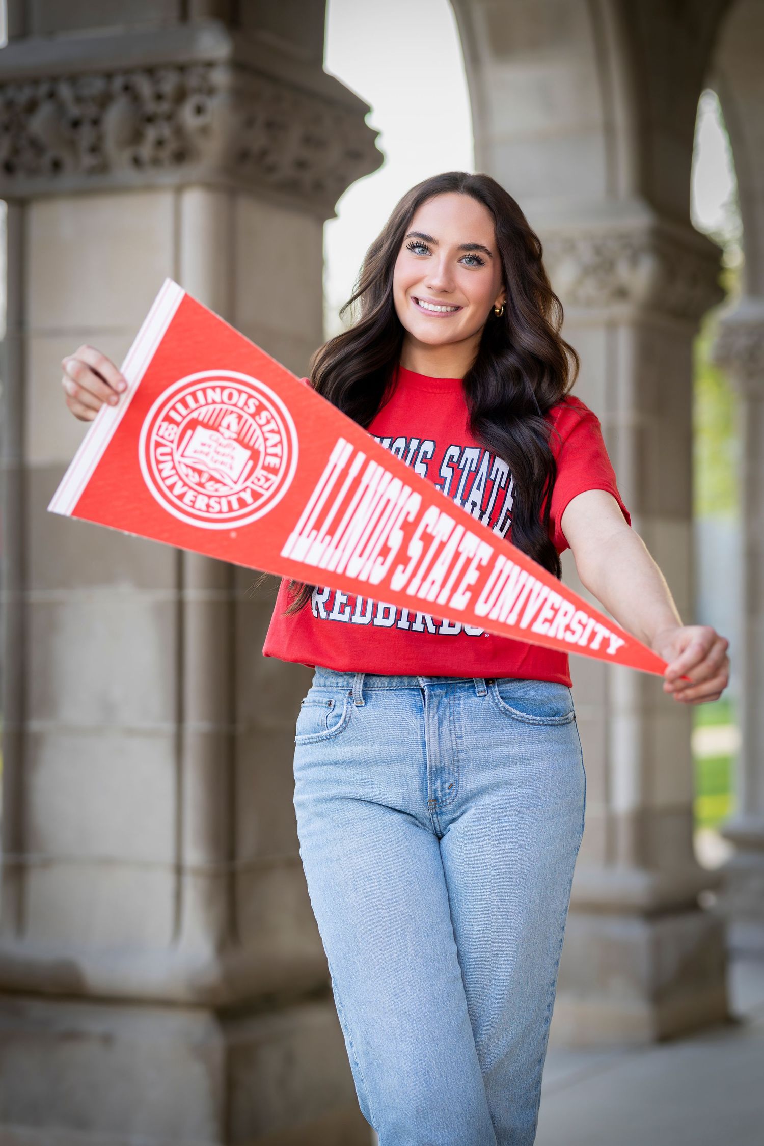 Smiling young woman holding Illinois State University Redbirds pennant and wearing red ISU t-shirt outdoors.