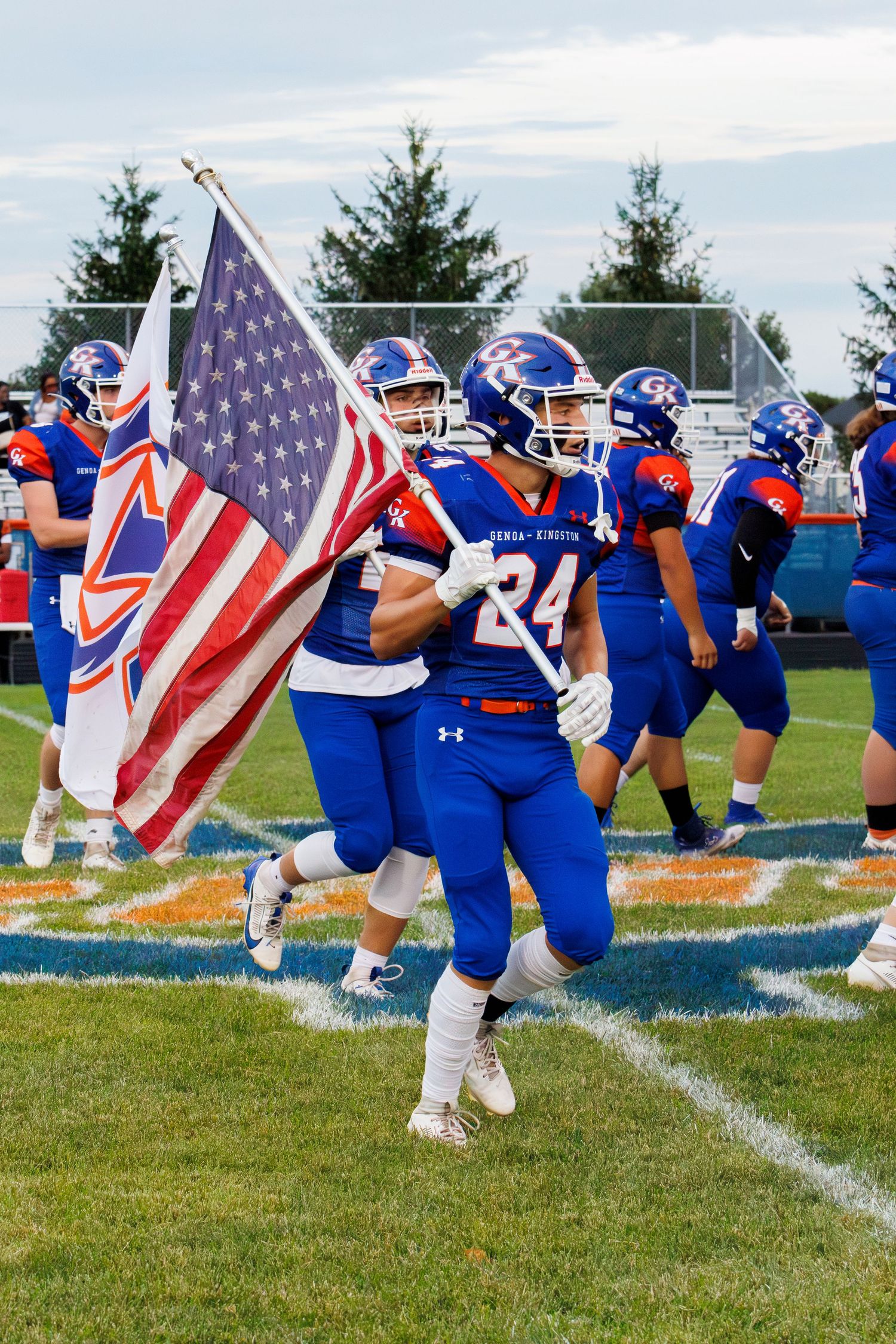 High school football player #24 carries American flag onto field before game.