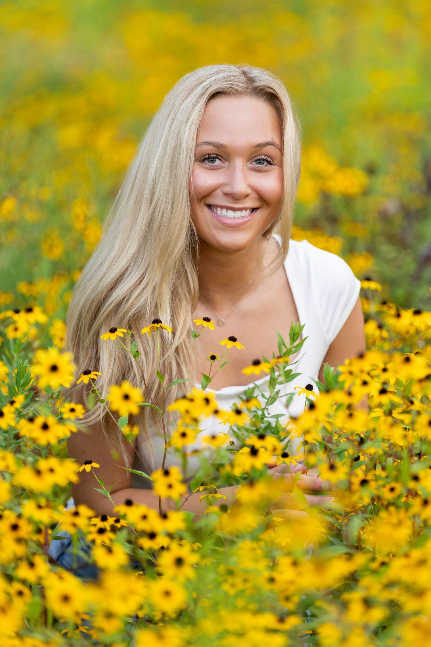 Smiling blonde woman lying in a vibrant field of yellow black-eyed Susan flowers on a sunny day.