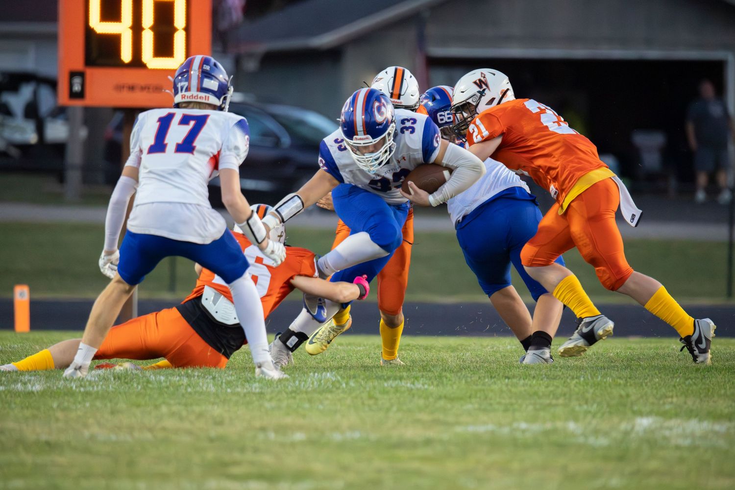 High school football players in blue and orange uniforms compete in an intense tackle during a Friday night game.