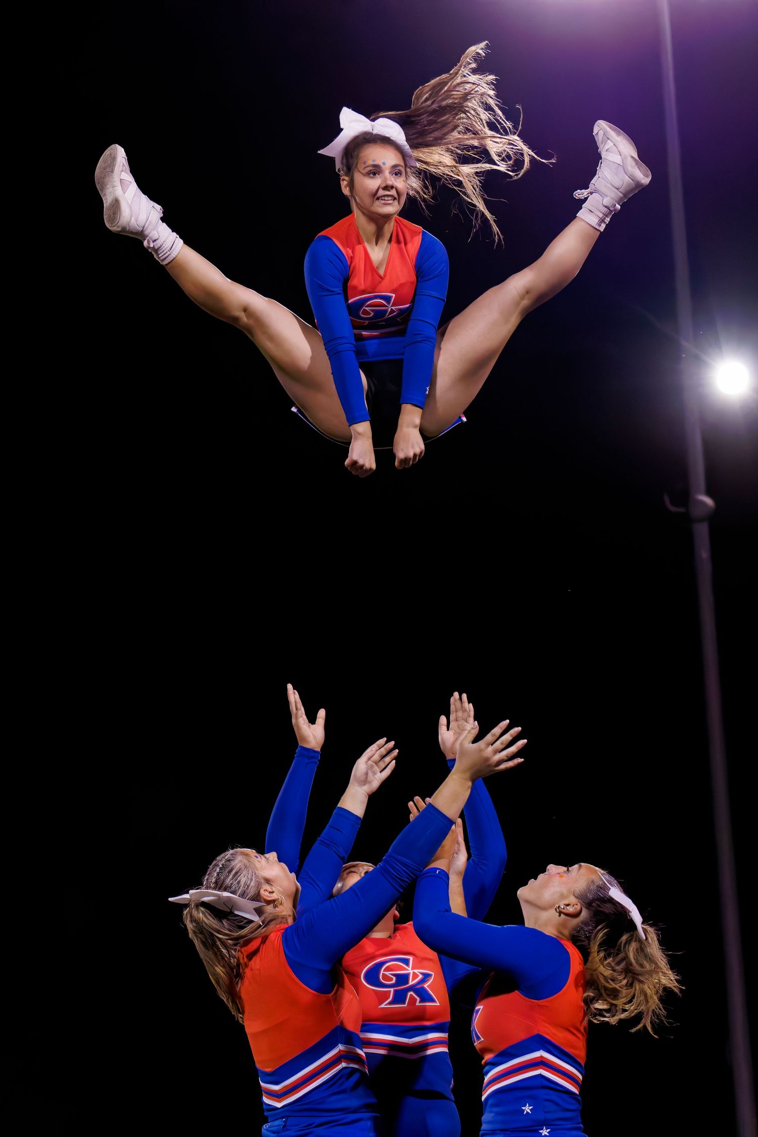 Cheerleaders perform a stunning stunt as a flyer soars mid-air in a split above her bases in blue and red uniforms.