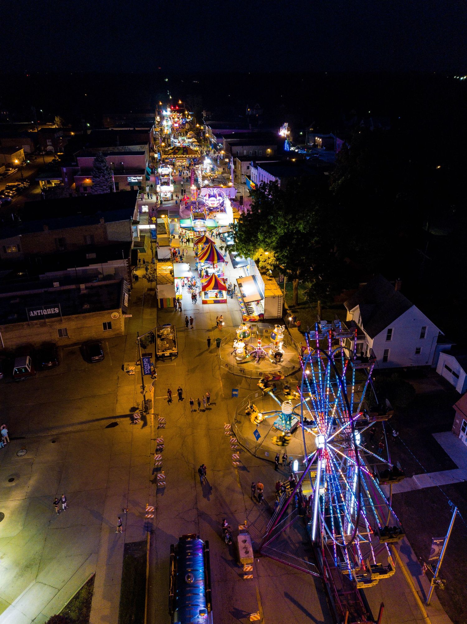Aerial night view of a vibrant county fair with colorful Ferris wheel and illuminated midway attractions.