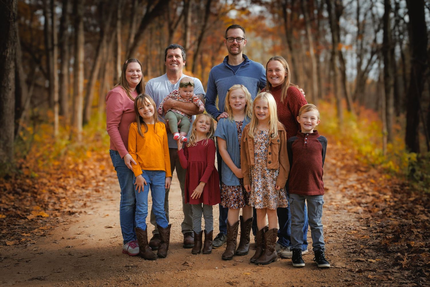 Family of nine posing on a scenic autumn forest trail surrounded by colorful fall foliage.