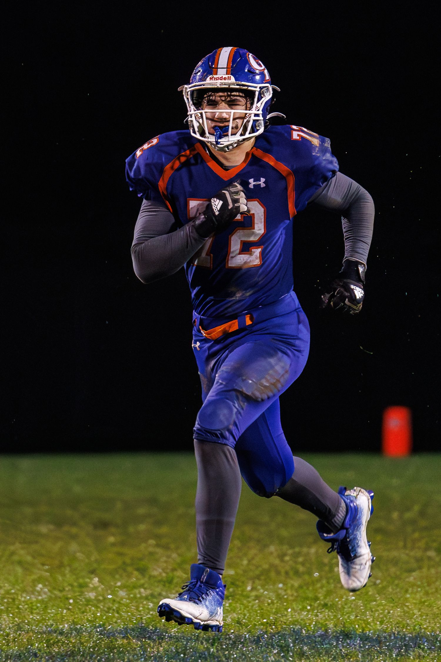 Football player #72 in blue and orange uniform running on field during night game.