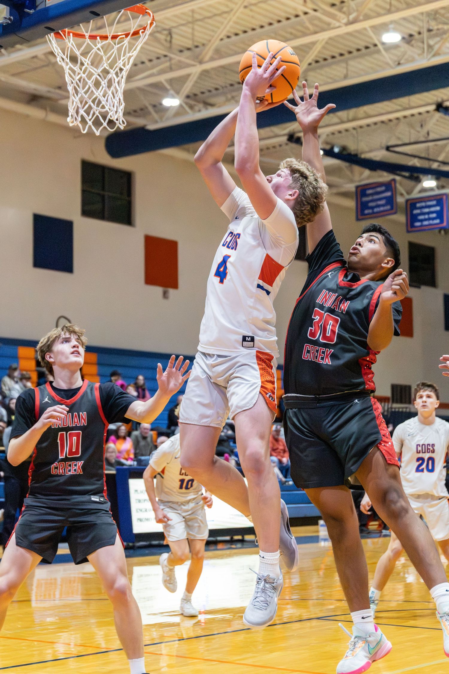 High school basketball player #4 in white leaps for layup against defender #30 in black during indoor game.