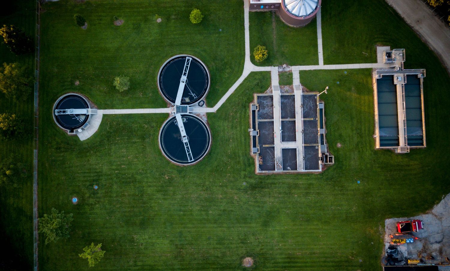 Aerial view of a water treatment facility with circular clarifiers and solar panels on lush green grounds.