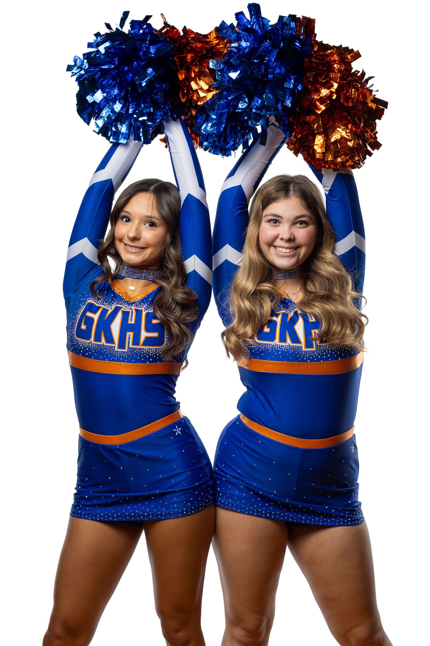 Two GKHS cheerleaders in blue and orange uniforms hold colorful pom-poms overhead, smiling against a white background.