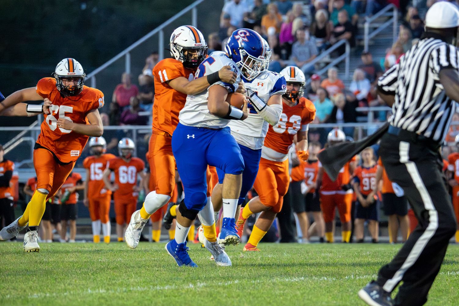 Football player in blue uniform breaks through tackle during high school game.