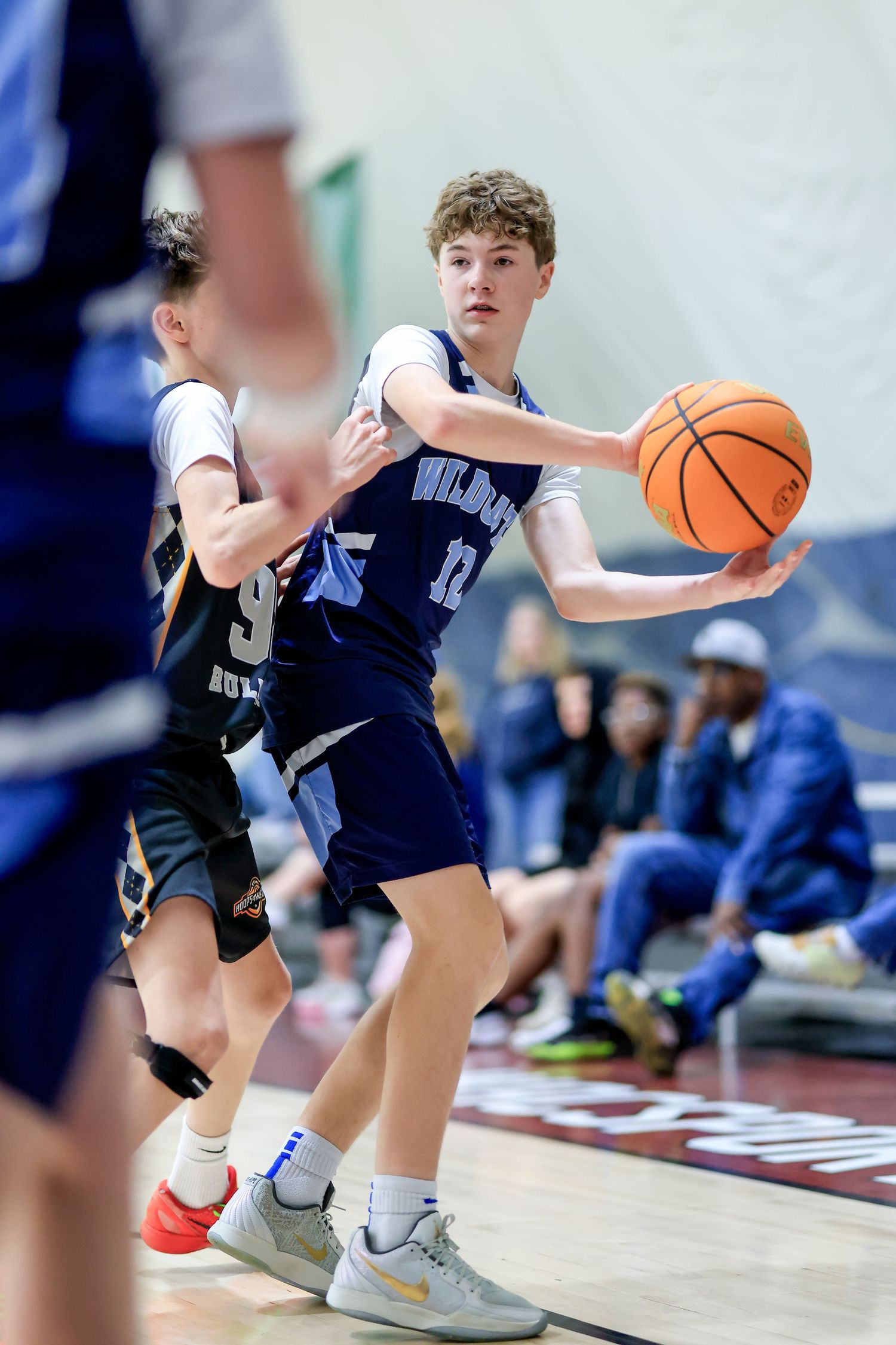 Young basketball player in blue Wildcats jersey handles the ball during an indoor youth basketball game.