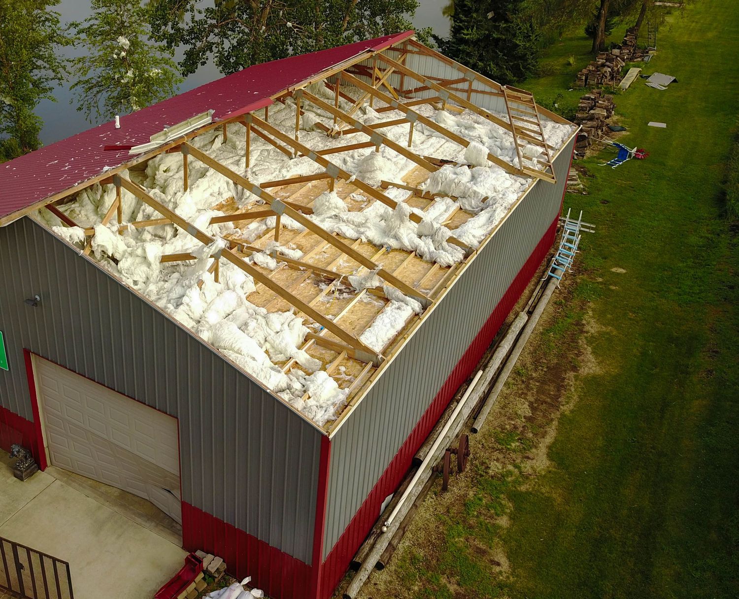 Aerial view of a storm-damaged metal building with roof rafters exposed and insulation debris scattered inside.