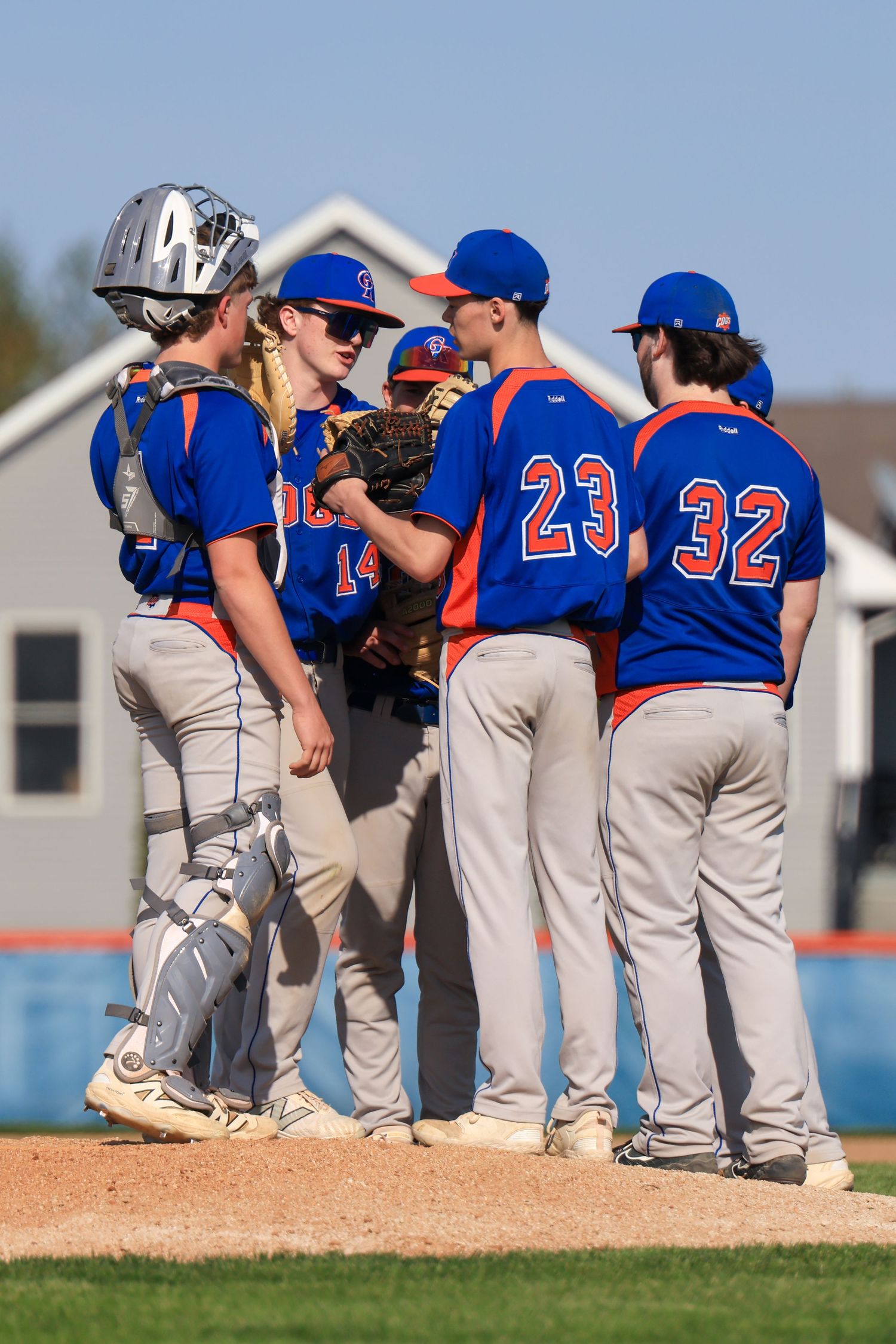 High school baseball team huddles on the pitching mound in blue and orange uniforms during a game.