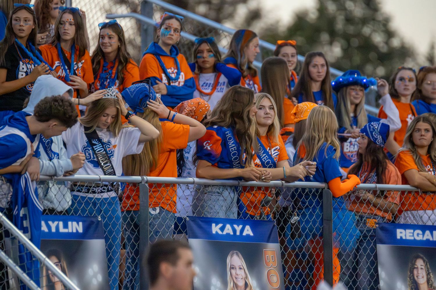 High school football fans in blue and orange cheer from the stands.