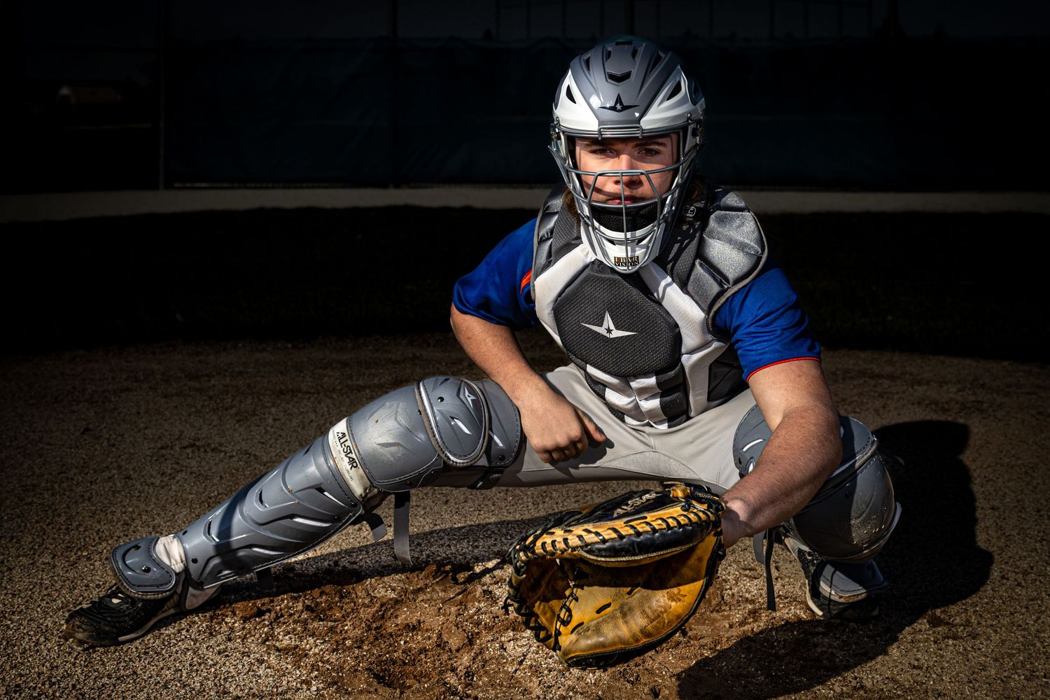 Baseball catcher in protective gear demonstrates low stance position during practice.