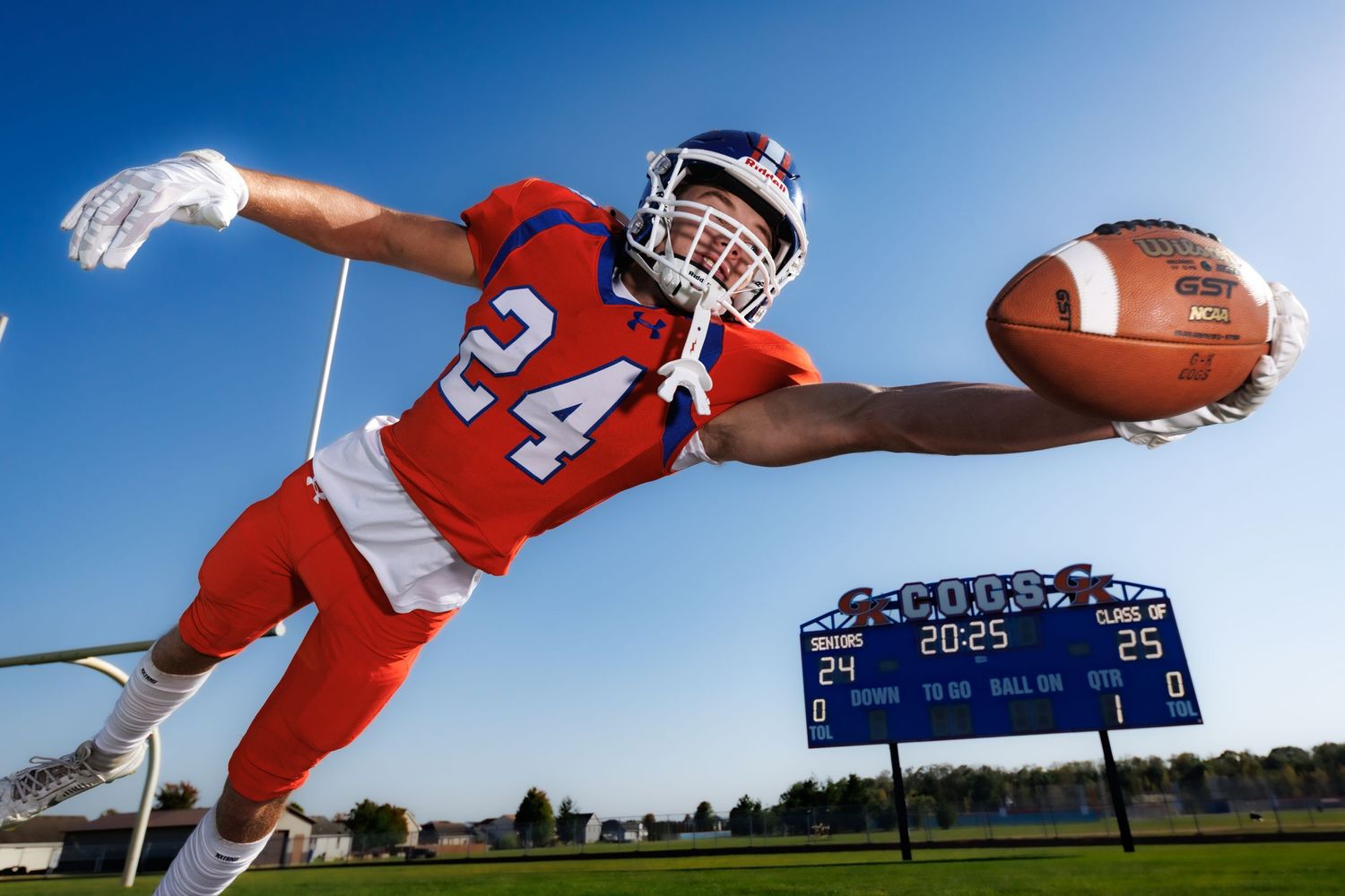 Football player in red uniform makes a diving catch during a game under blue sky.