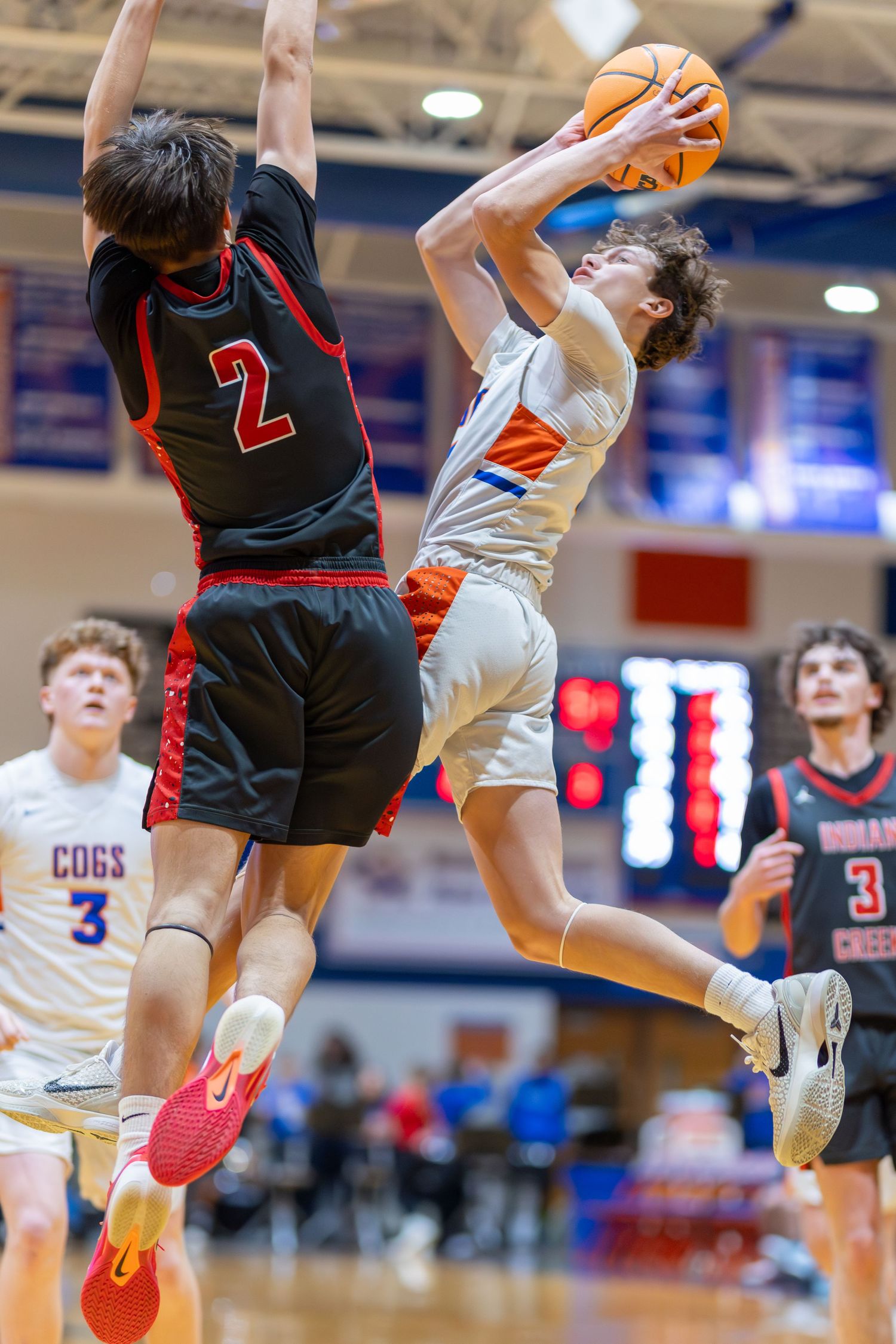 A basketball player in white jumps to shoot over a defender in black jersey number 2 during a high school game.