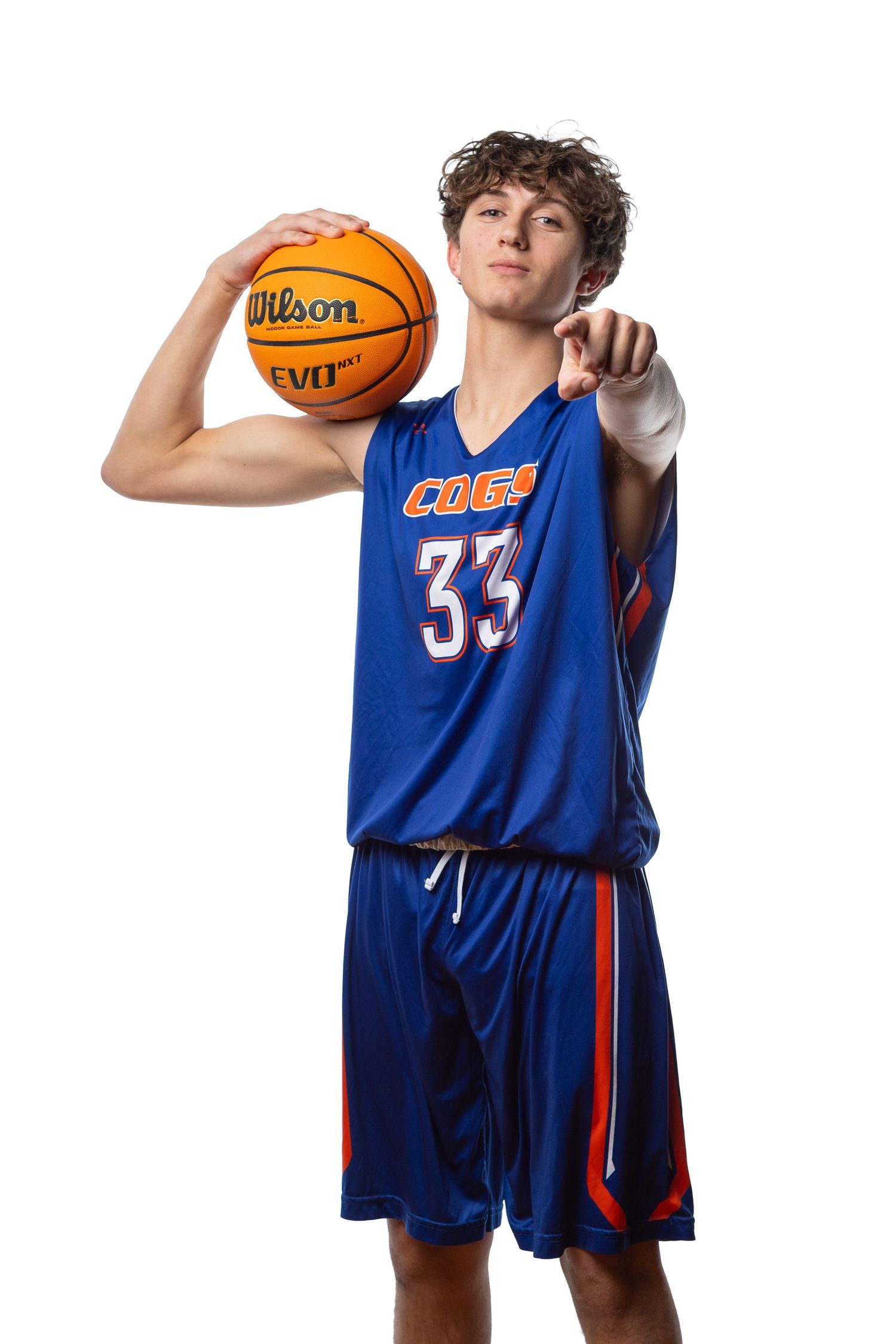 Young basketball player in blue number 33 jersey holding a Wilson ball, pointing at camera on white background.