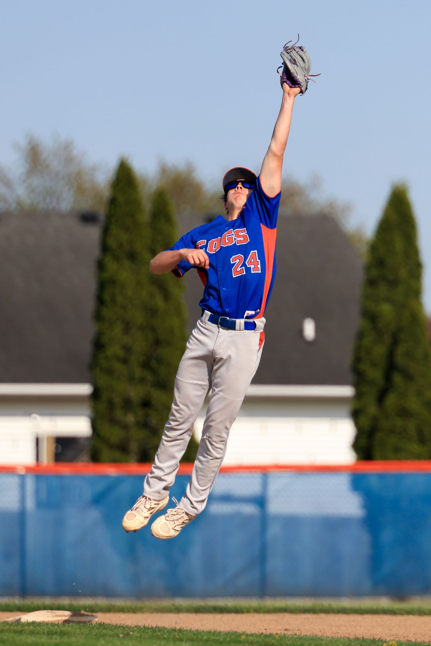 Baseball player number 24 in blue uniform leaps high to catch a ball with outstretched glove.