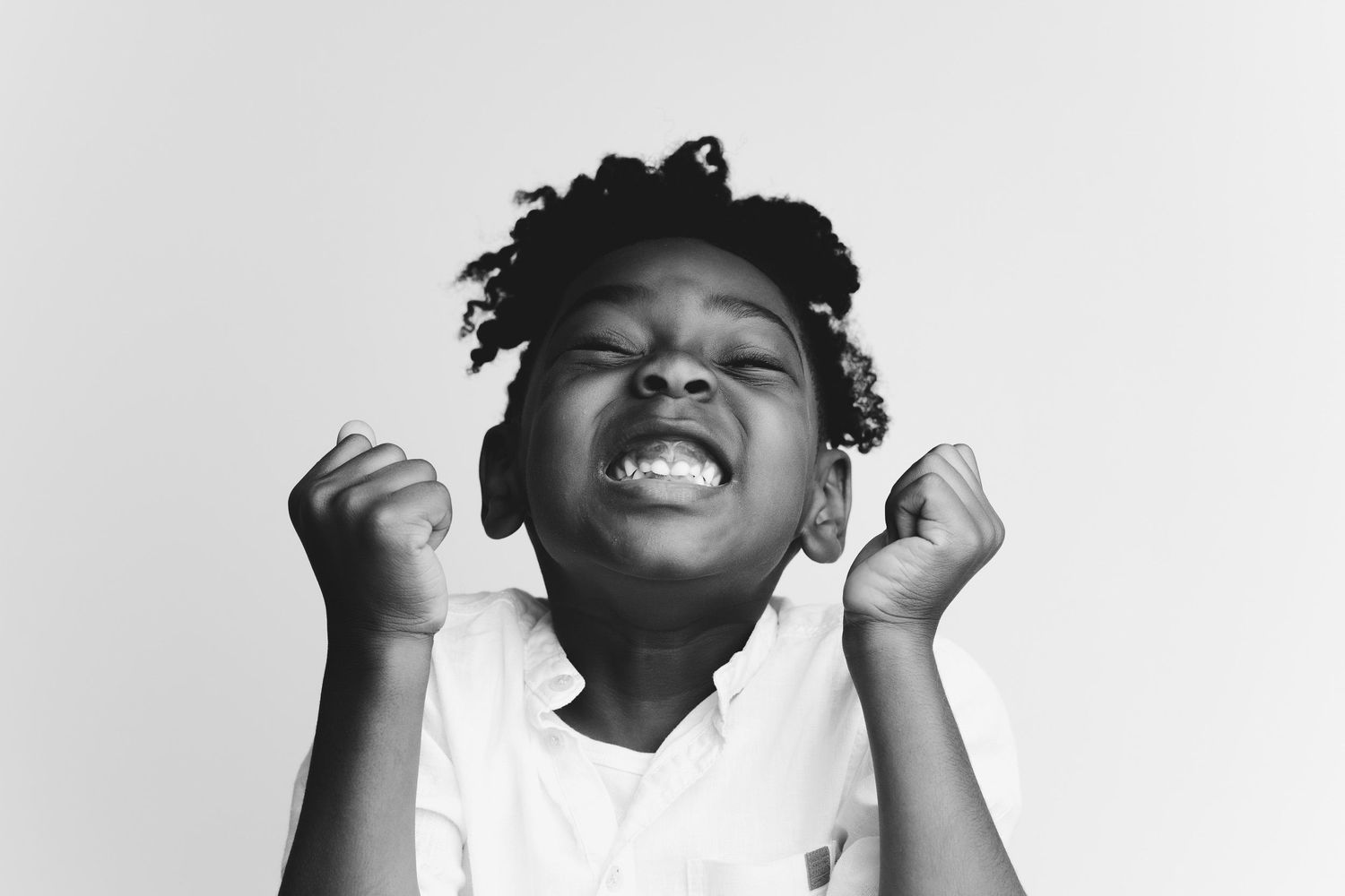 Black and white portrait of a joyful child with closed eyes and raised fists expressing pure excitement.