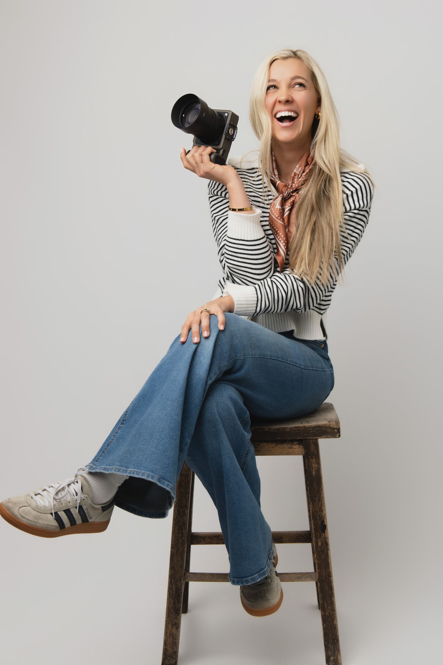 A person in a striped top and jeans sits casually on a wooden stool against a white background in various poses.