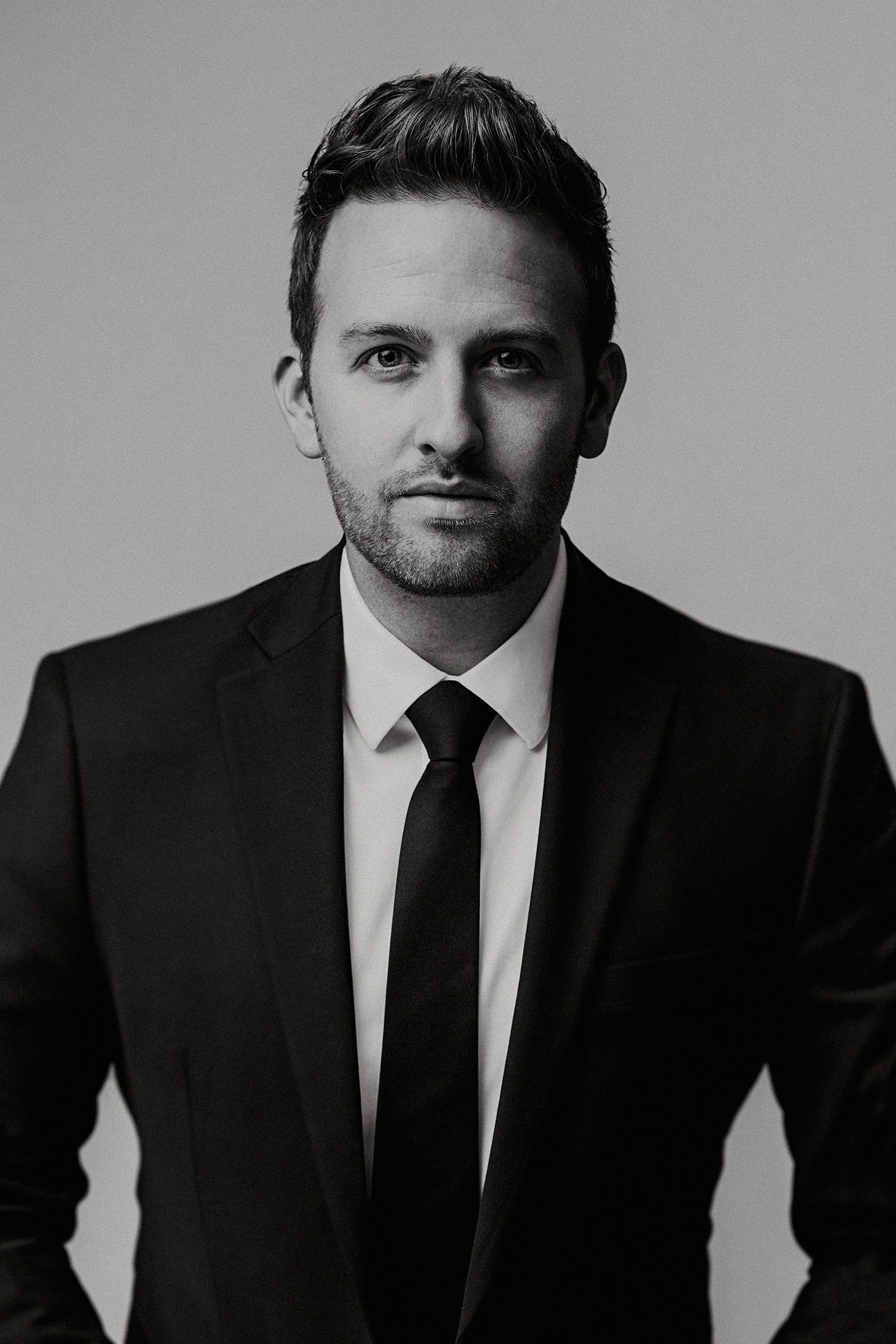 Professional black and white studio portrait of a person in a dark suit and tie against a plain background.