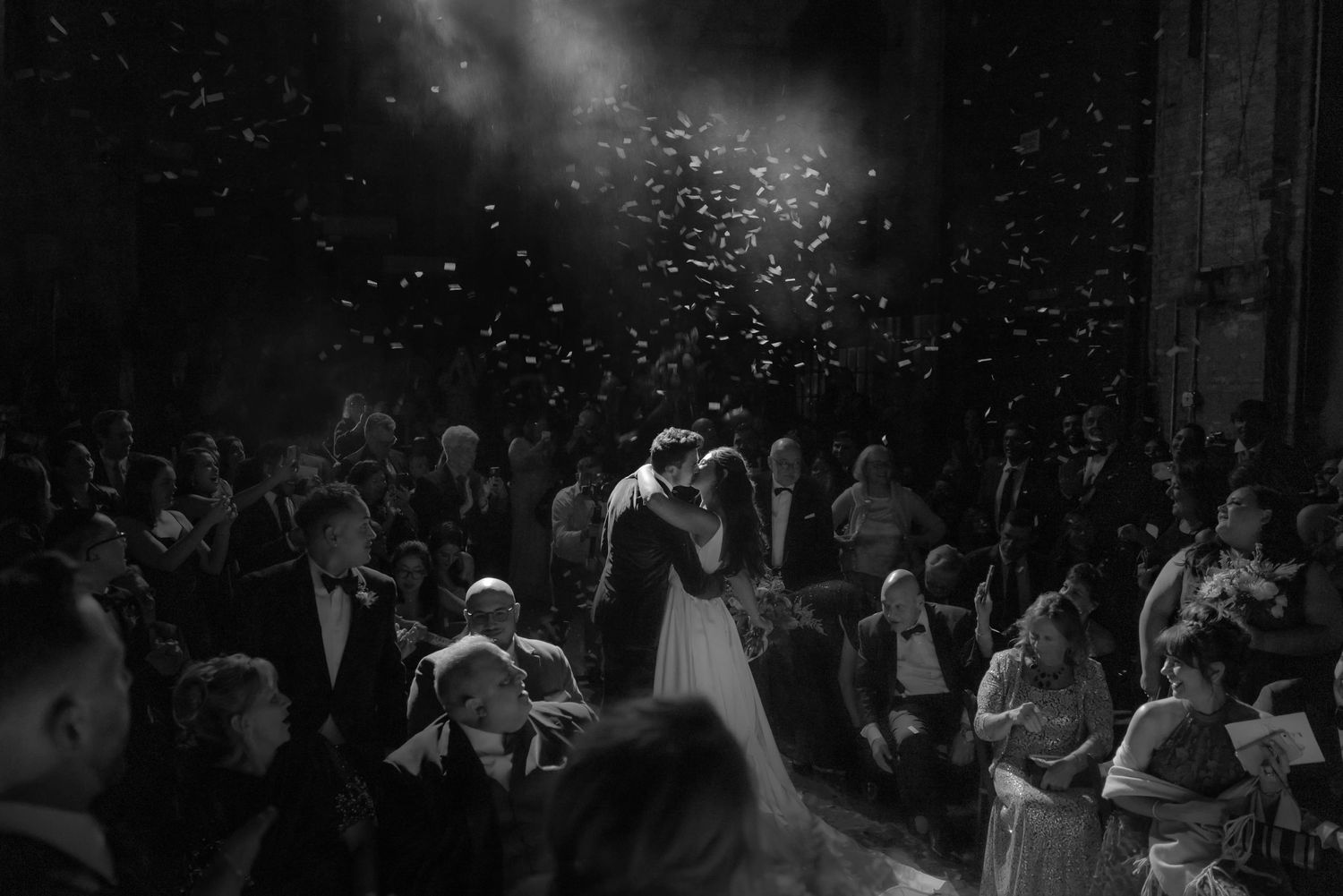 Black and white wedding celebration photo with confetti falling in dramatic lighting.
