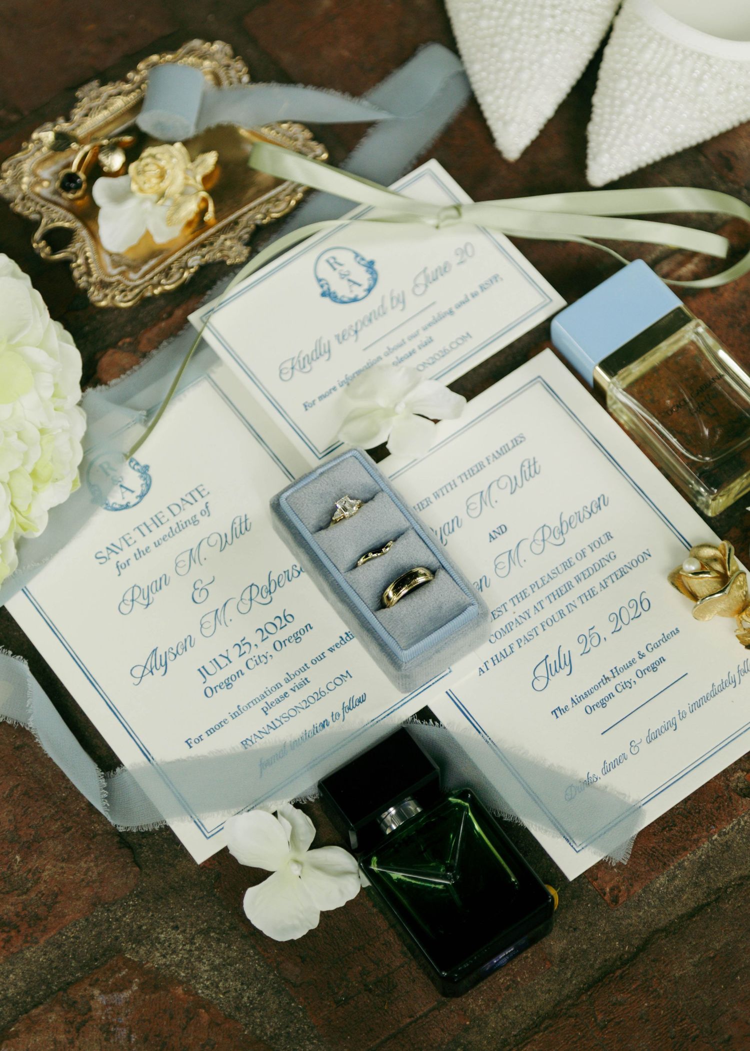 Elegant wedding invitation suite with dusty blue accents, rings, and floral details for a July 2026 ceremony in Oregon.