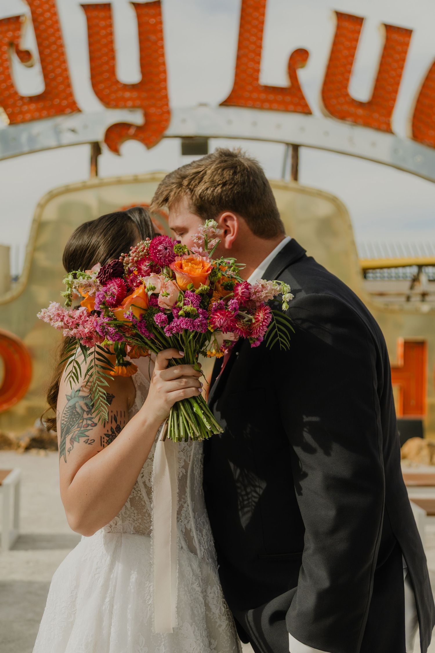 Bride and groom kissing behind a vibrant pink and orange wedding bouquet at the Neon Museum in Las Vegas.