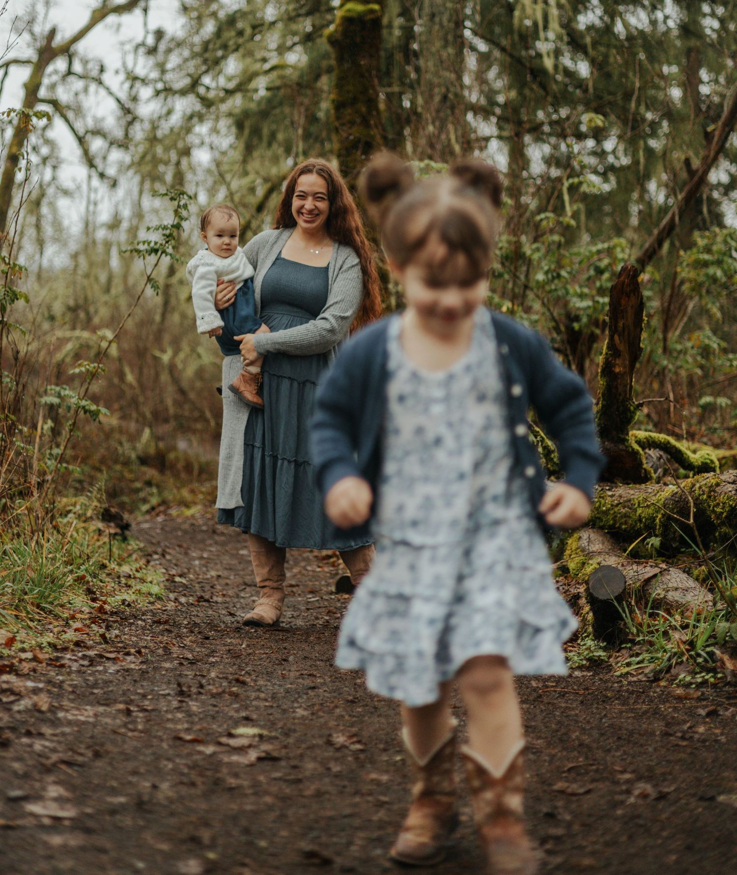A family enjoys a walk together on a mossy forest trail on an overcast day.