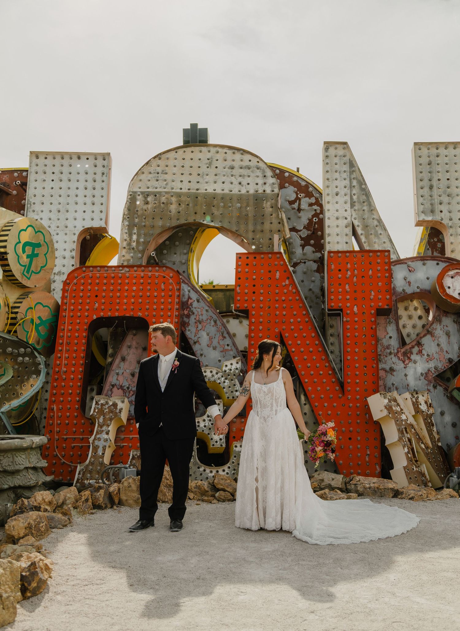 Bride and groom hold hands in front of vintage neon signs at the Neon Museum in Las Vegas on their wedding day.