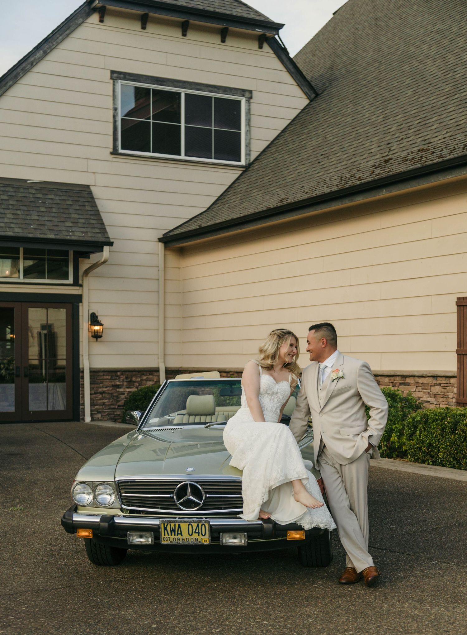 Bride and groom posing with a vintage Mercedes-Benz convertible in front of an elegant venue.
