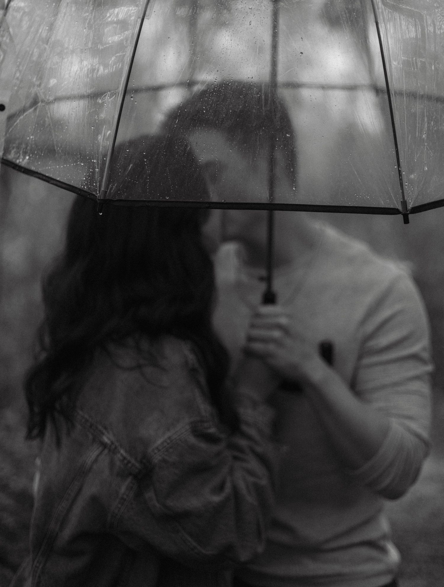 A silhouetted couple shares a romantic moment under a clear umbrella.