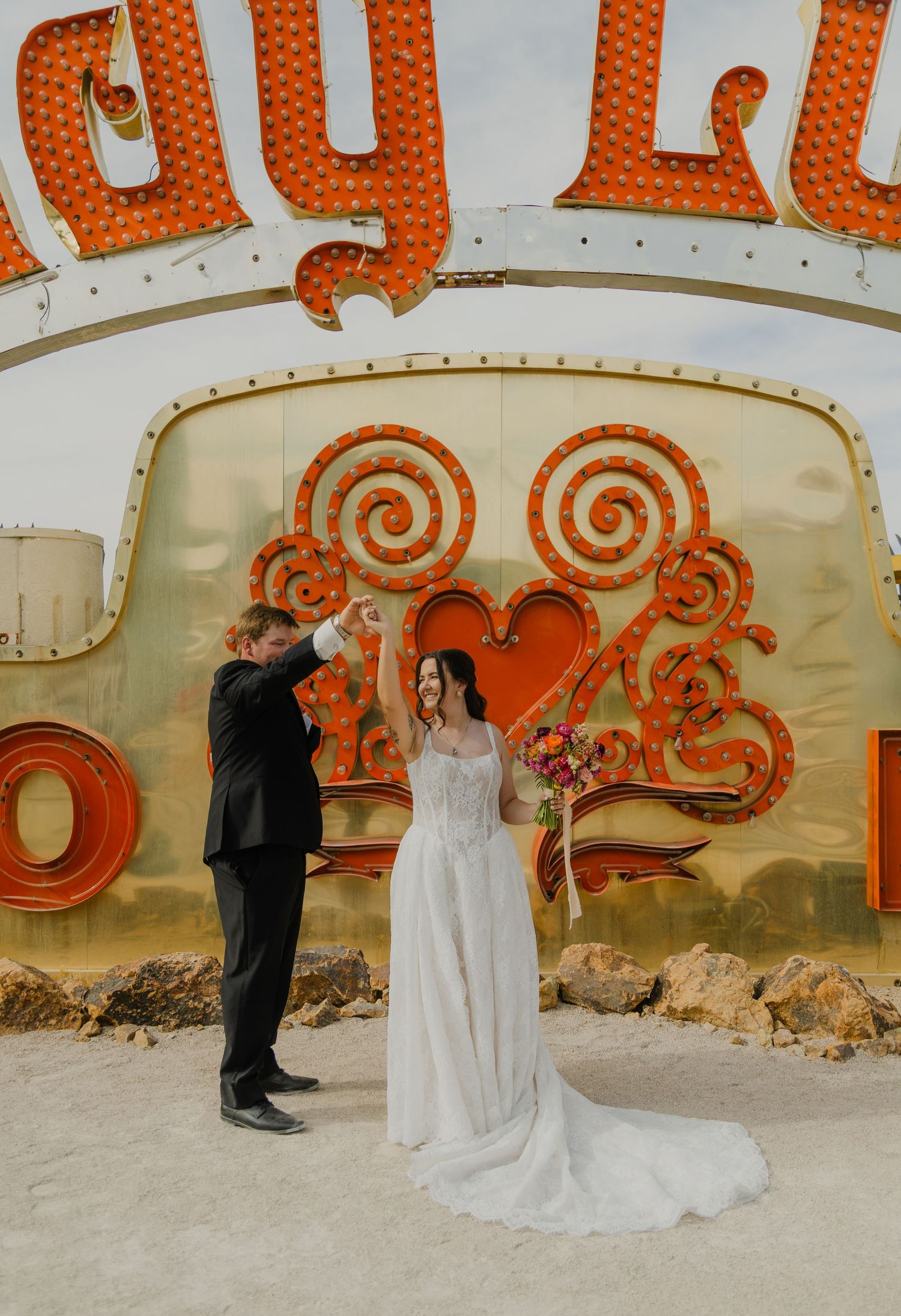Couple dancing in front of colorful vintage neon signs at the Neon Museum in Las Vegas, bride in white gown holding bouquet.