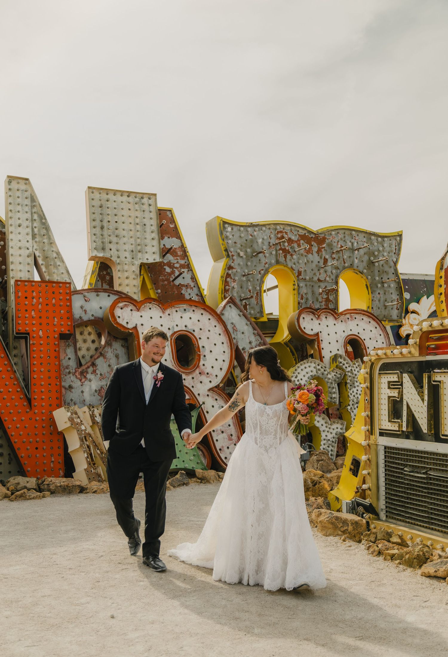 Bride and groom walk hand-in-hand among colorful vintage neon signs at the Neon Museum in Las Vegas.