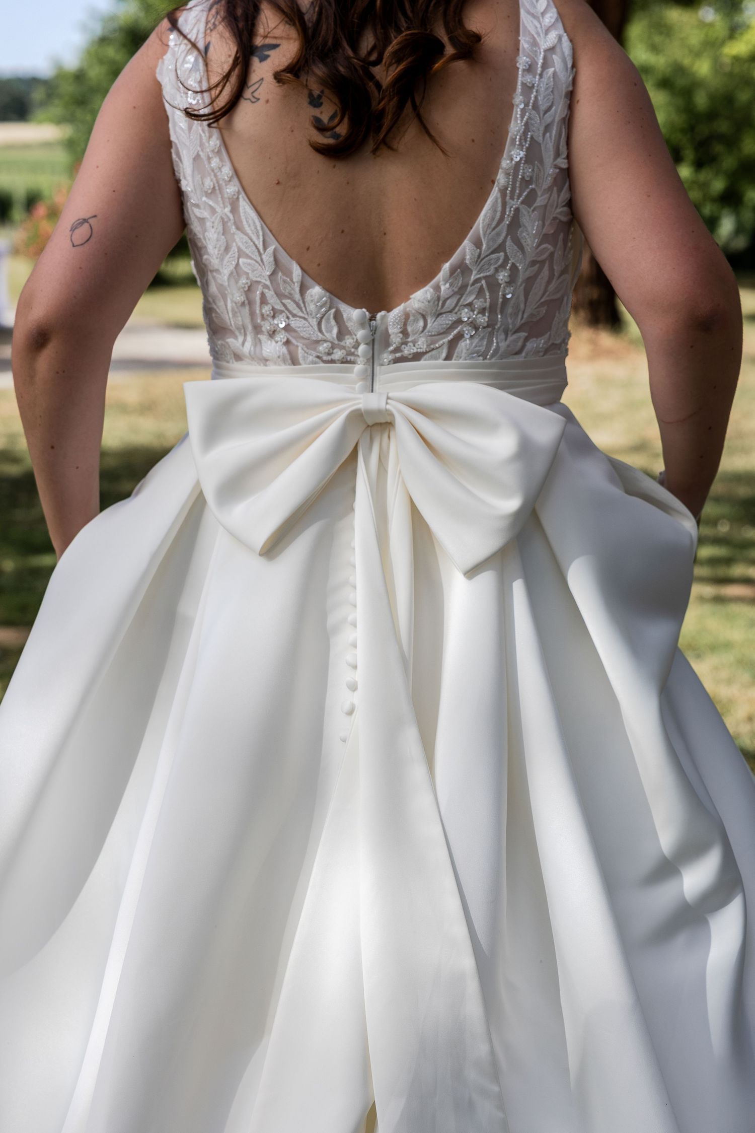 Back view of a bride in a white wedding gown with lace bodice, low back, and large satin bow at the waist.