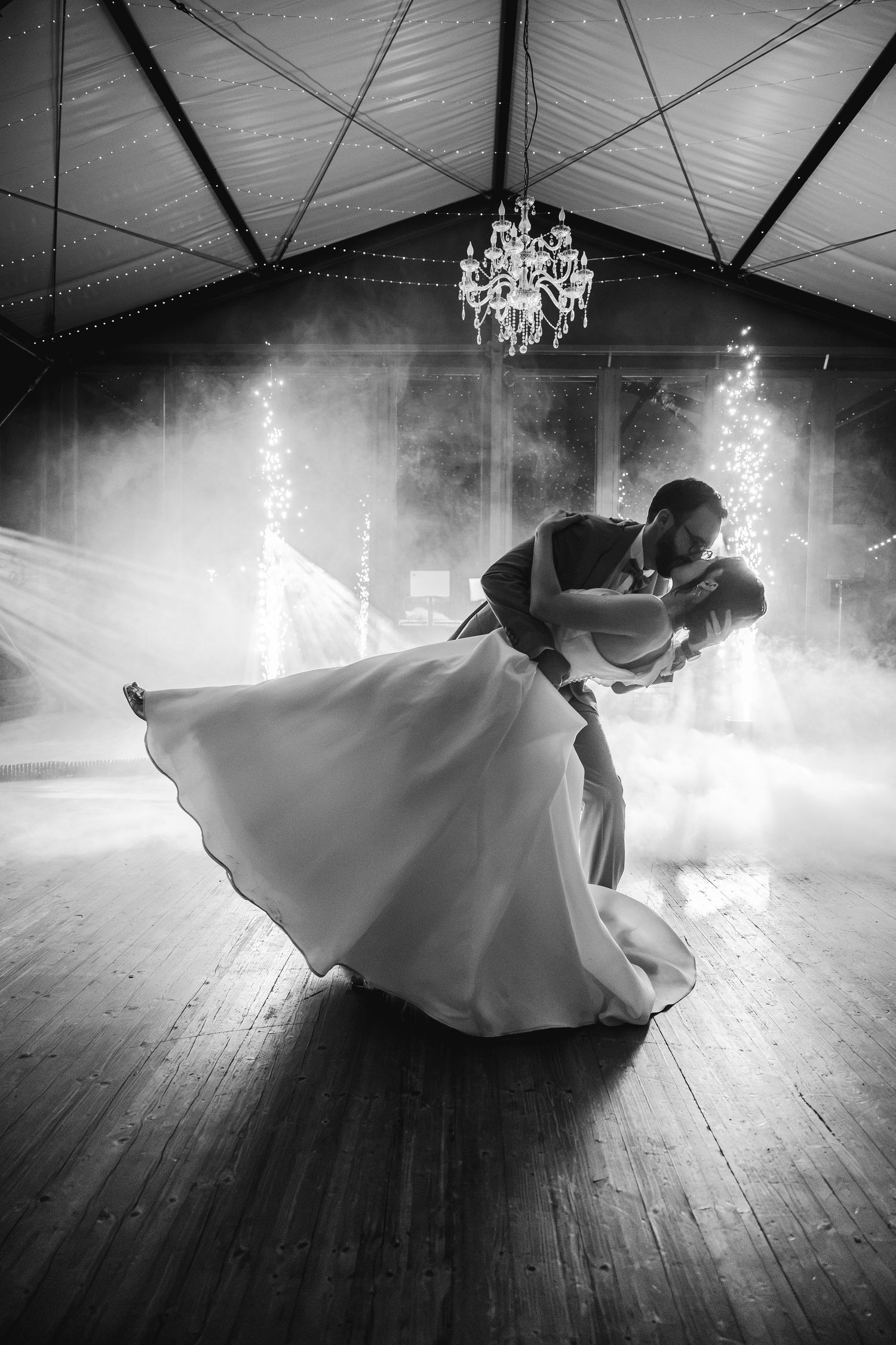 Bride and groom share a romantic dip during their first dance in a softly lit wedding venue.