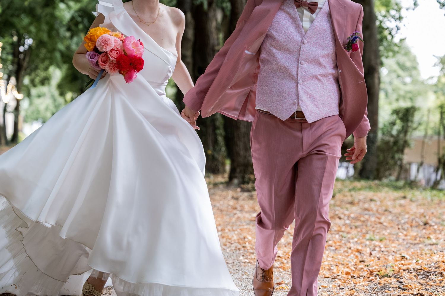 Bride in white gown and groom in pink suit walking hand in hand outdoors at their wedding.